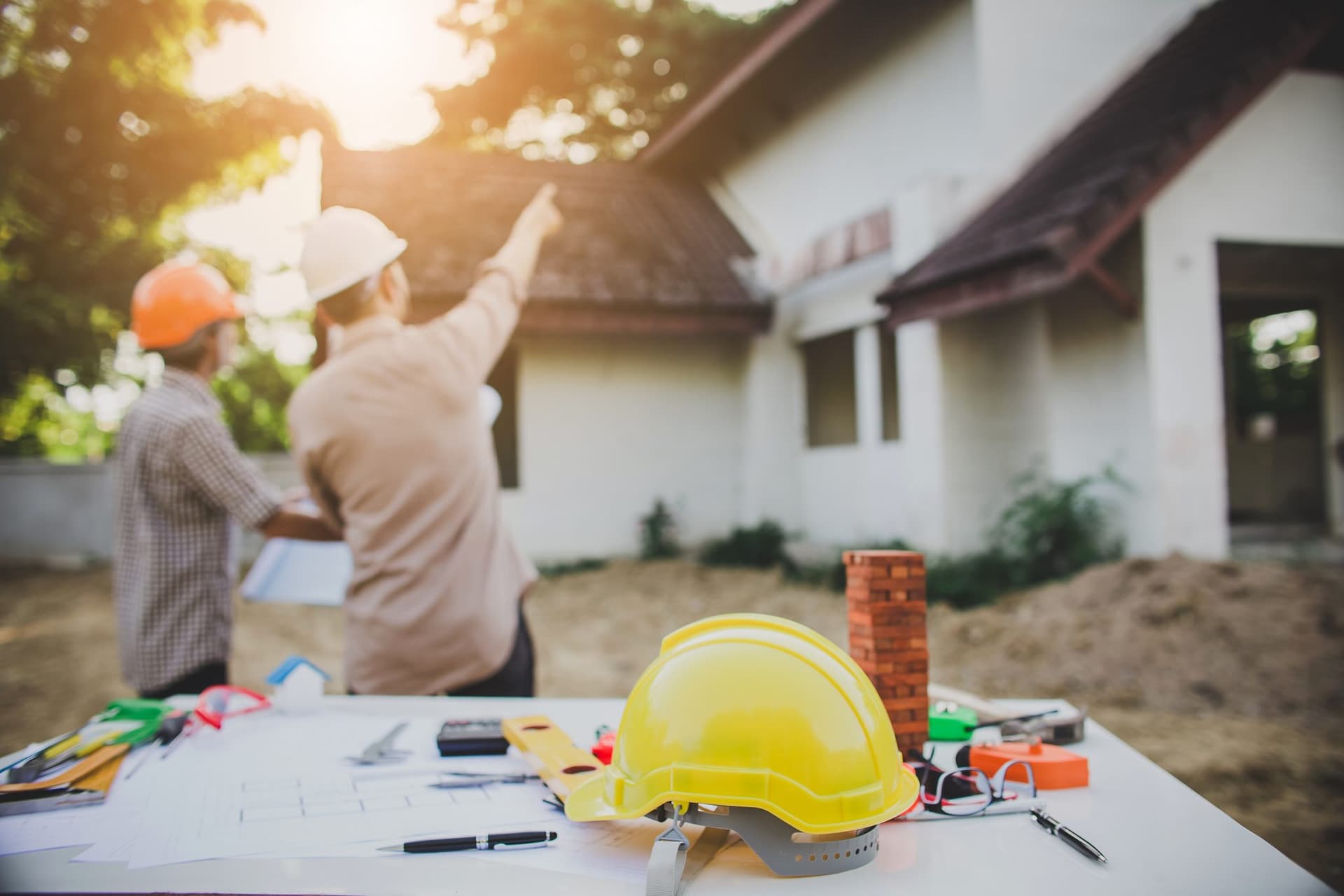 Deux techniciens en repérage devant une maison en chantier, plans et casque de sécurité au premier plan